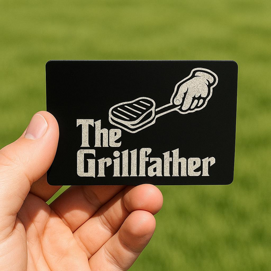 Card with 'The Grille father' design held by a hand against a freshly cut lawn background