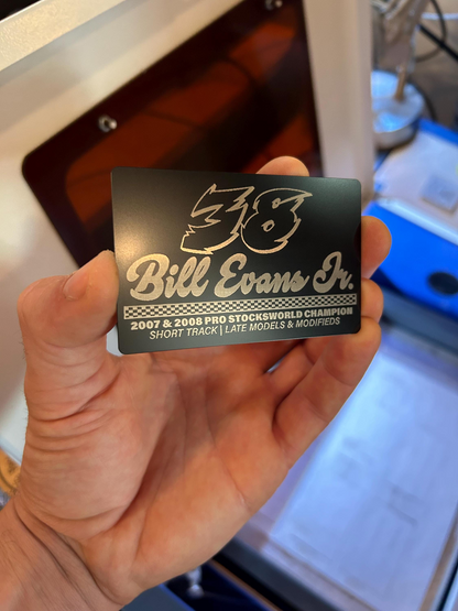 Hand holding a laser engraved custom metal business card with race car driver design, with car number and sponsors in black/silver anodized aluminum