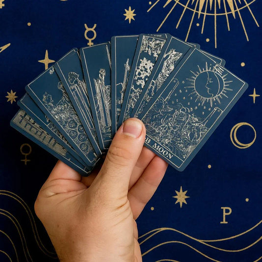 Hand holding tarot cards against a dark blue background with star and moon symbols
