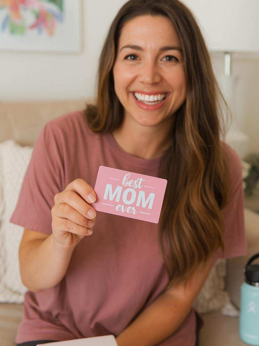 Woman holding a metal laser engraved business card with 'best mom ever' text in a home setting