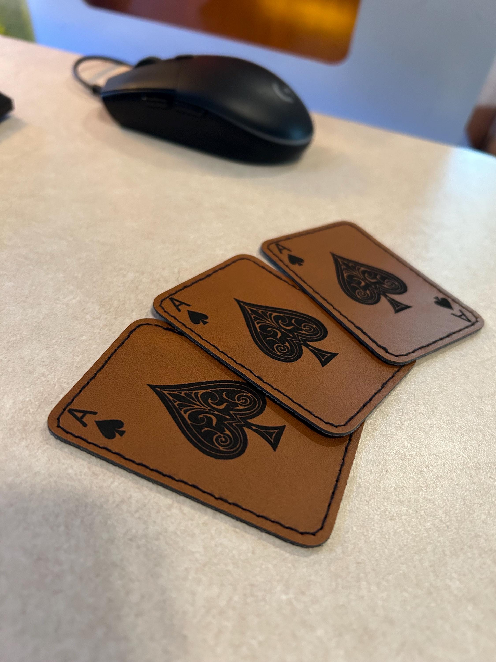 Three brown leather ace of spades patches on a flat surface with computer mouse in background for size reference