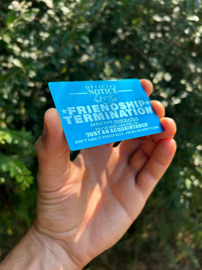 Hand holding a blue metal gift card with novelty humor text against a blurred green background