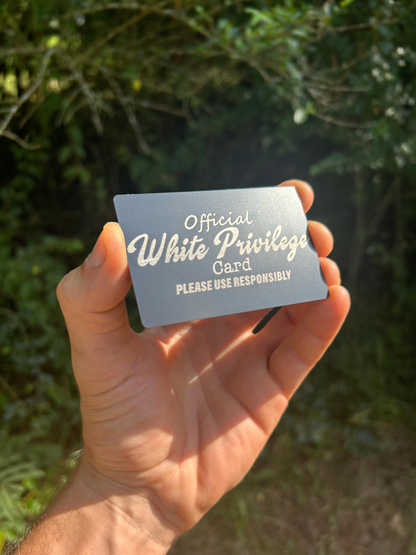 Hand holding a laser engraved gift with 'Official White Privilege Card' text against a blurred natural background