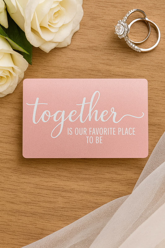 Pink card with 'Together is our favorite place to be' text, ring, and white roses on a wooden surface