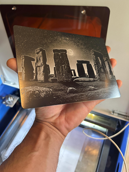 Metal decorative plaque with detailed laser engraved image of Stonehenge held by a hand.