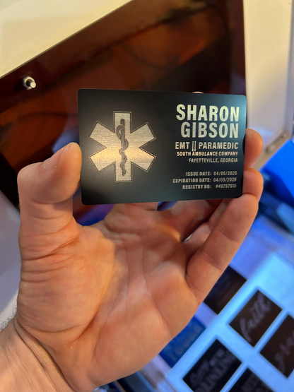 Hand holding a personalized metal business card with medical emergency services details.