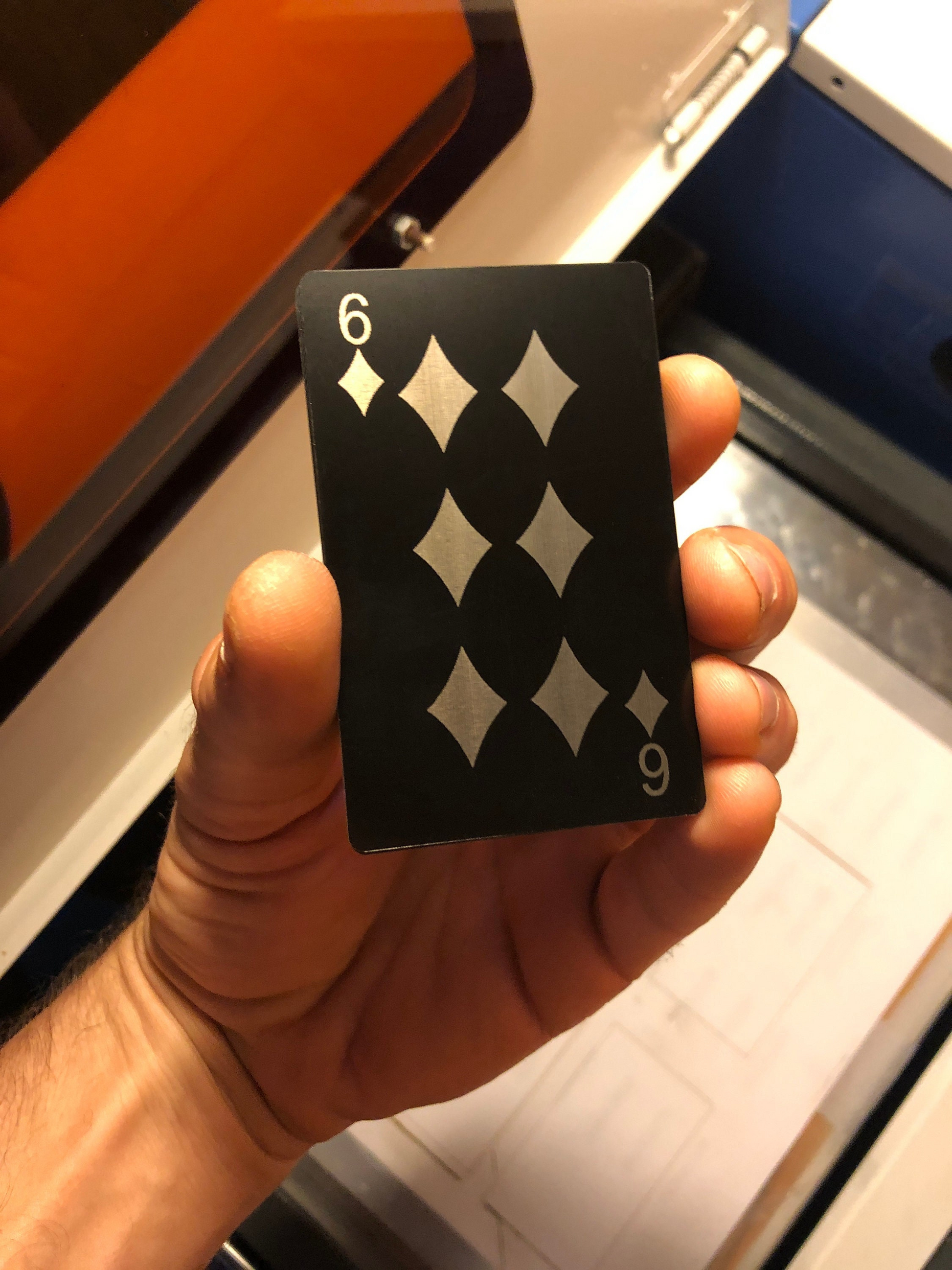 Hand holding a metal playing card with black background and silver six of diamonds laser engraving