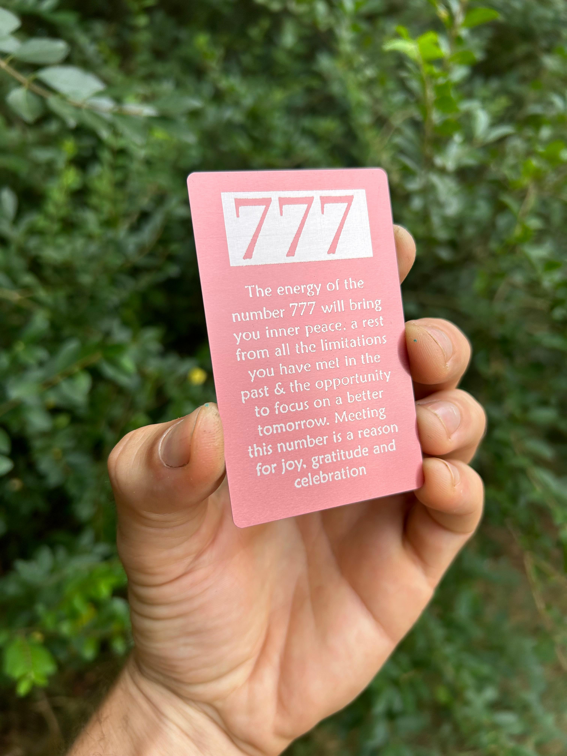Hand holding a pink card with '777' and spiritual energy text against a green leafy background