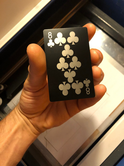 Hand holding a black metal eight of clubs playing card laser engraved in anodized aluminum
