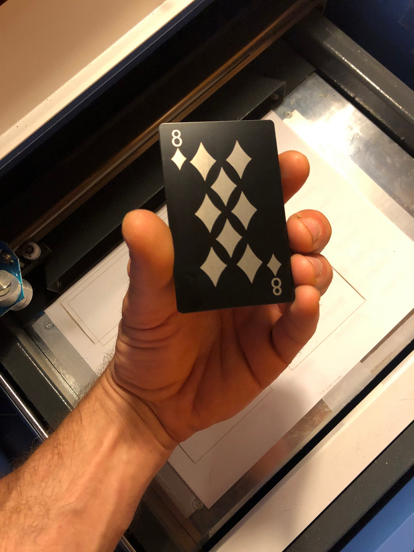 hand holding an anodized aluminum laser engraved poker card with 8 of diamonds design in front of a machine background