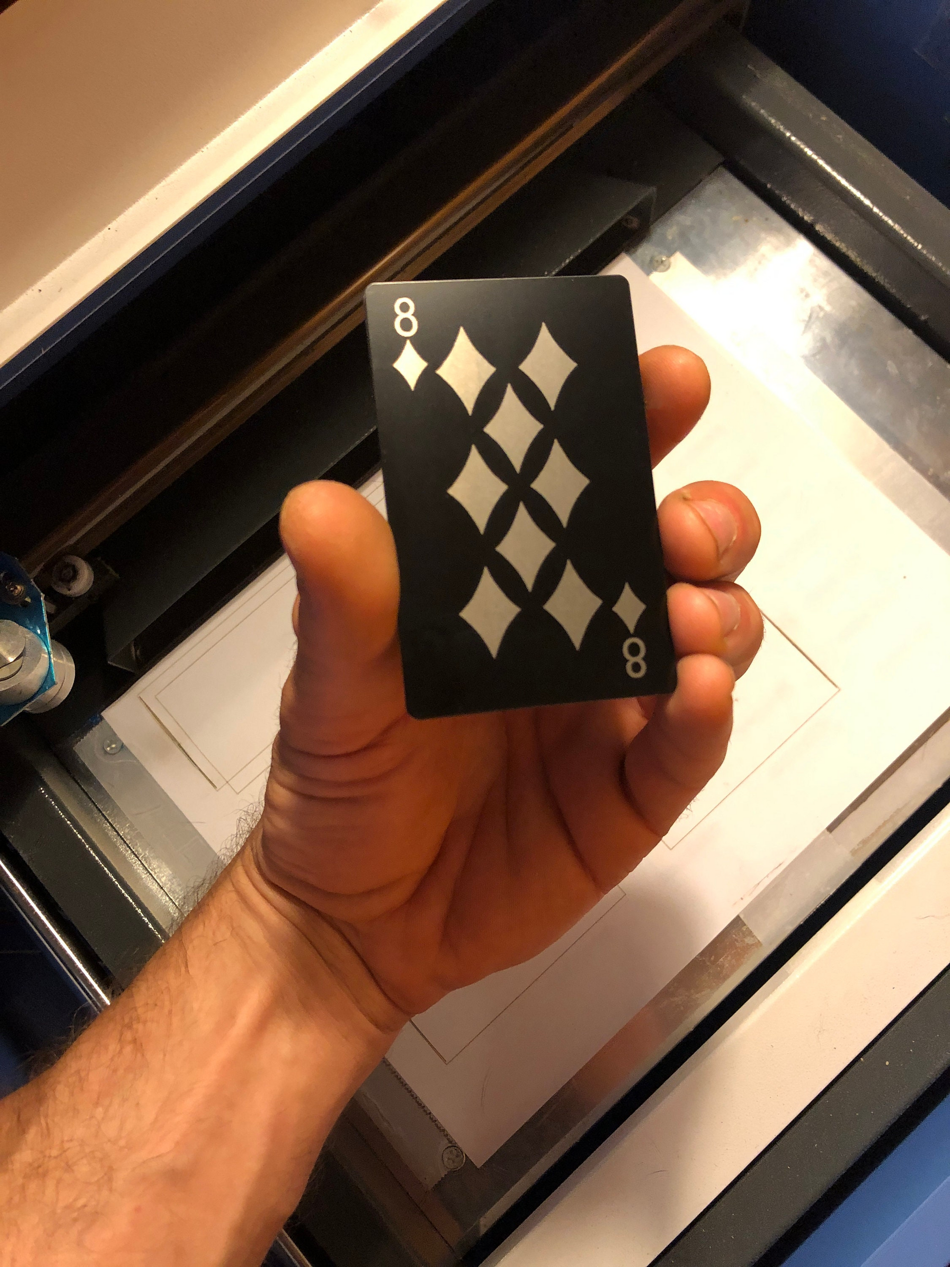 hand holding an anodized aluminum laser engraved poker card with 8 of diamonds design in front of a machine background