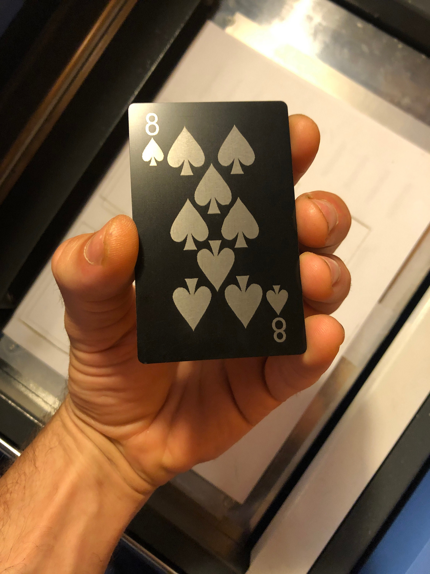 Hand holding a black metal 8 of spades playing card with silver symbols