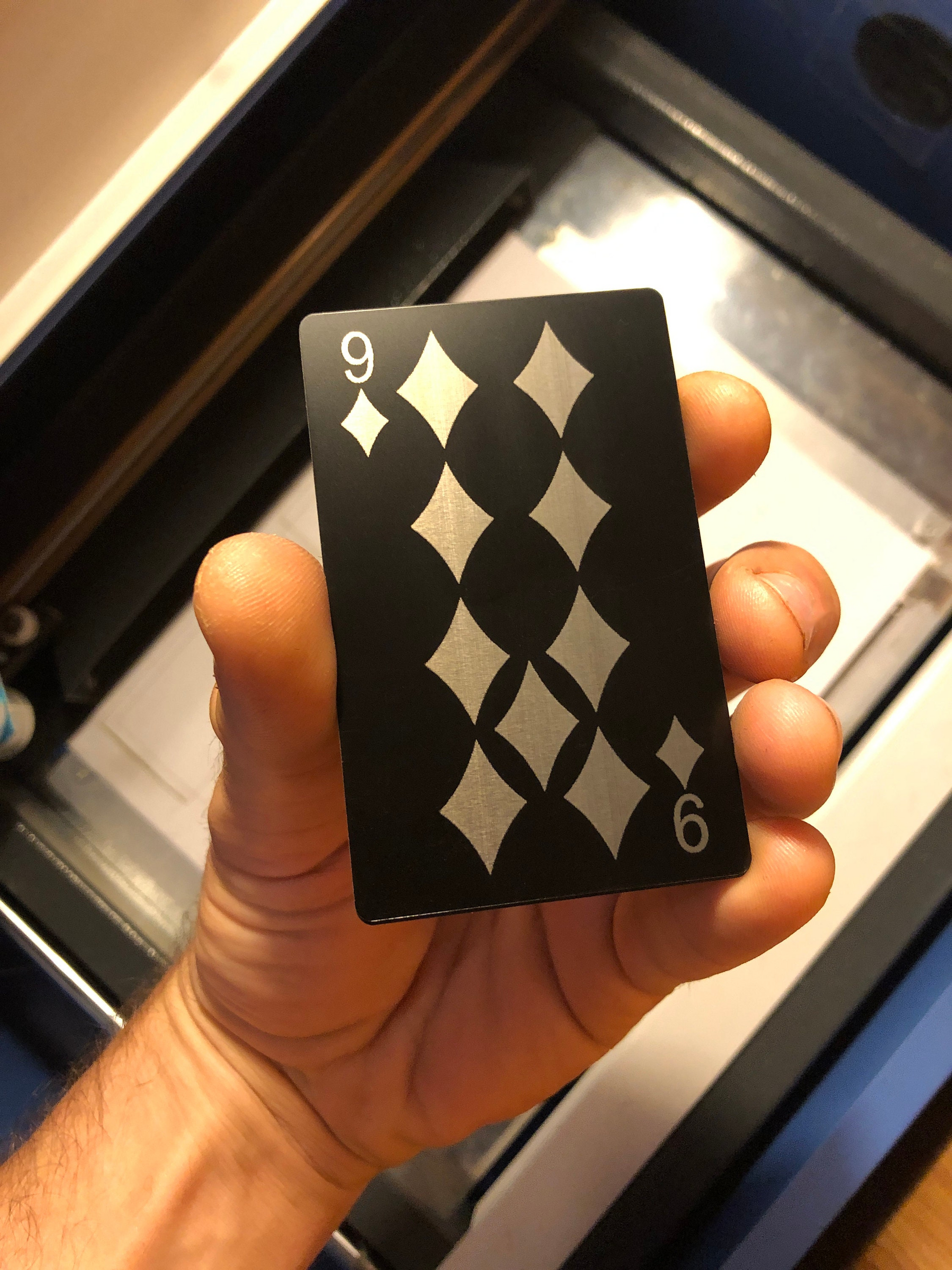 Hand holding a black metal playing card with nine of diamonds laser engraving