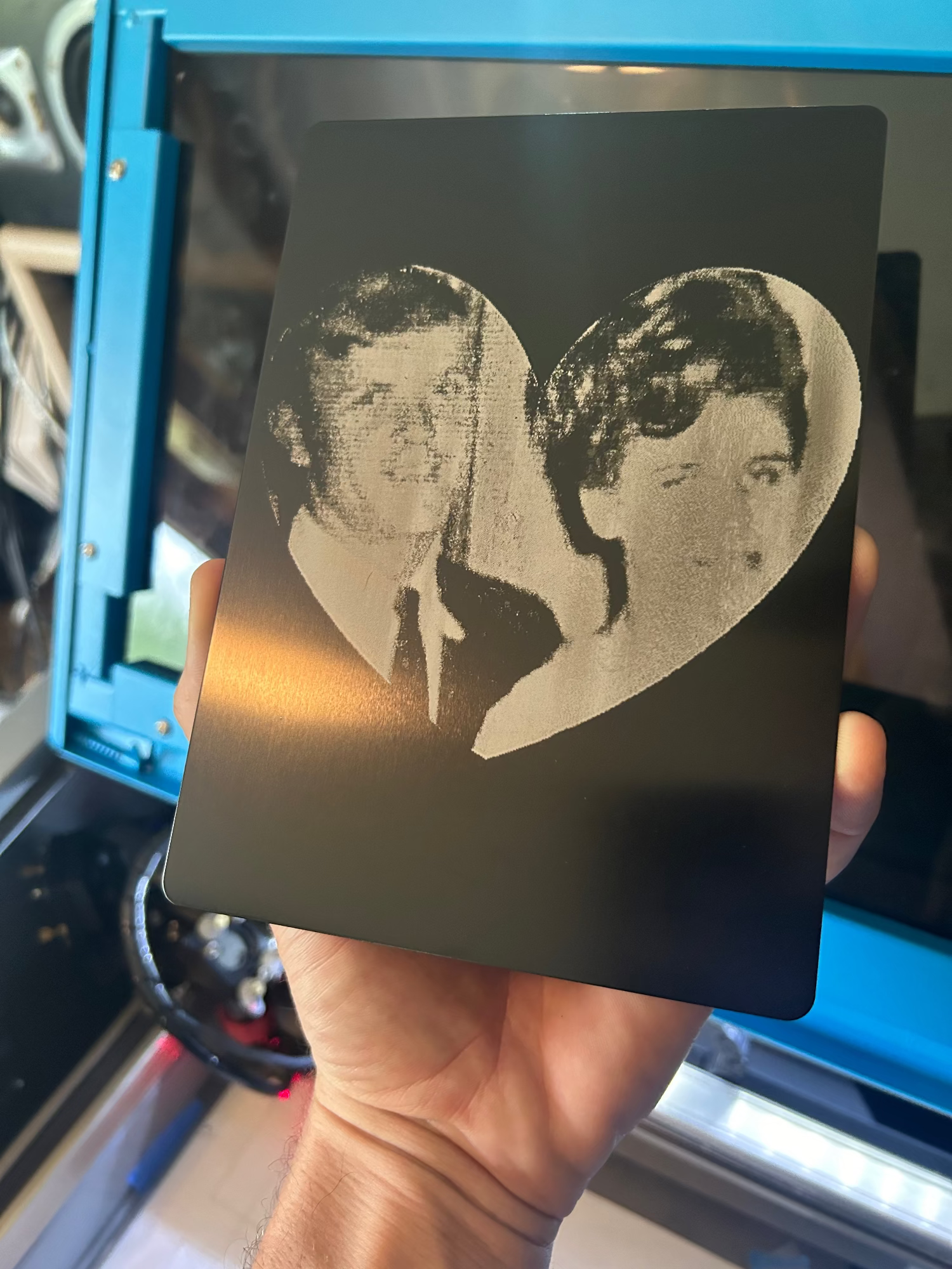 Hand holding a metal 5x7 with laser engraved portrait of a couple.