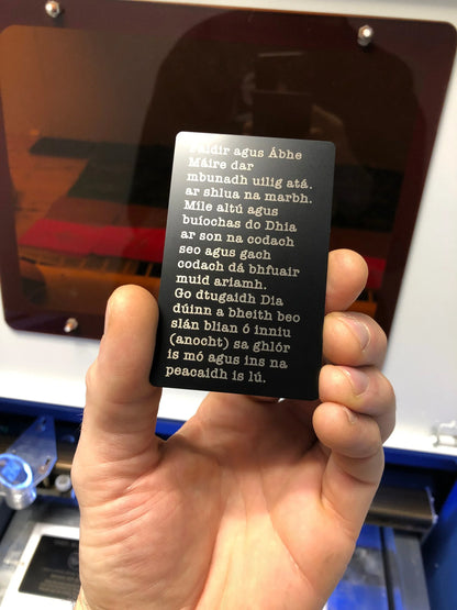 Hand holding a black engraved custom prayer card with white text against a blurred background