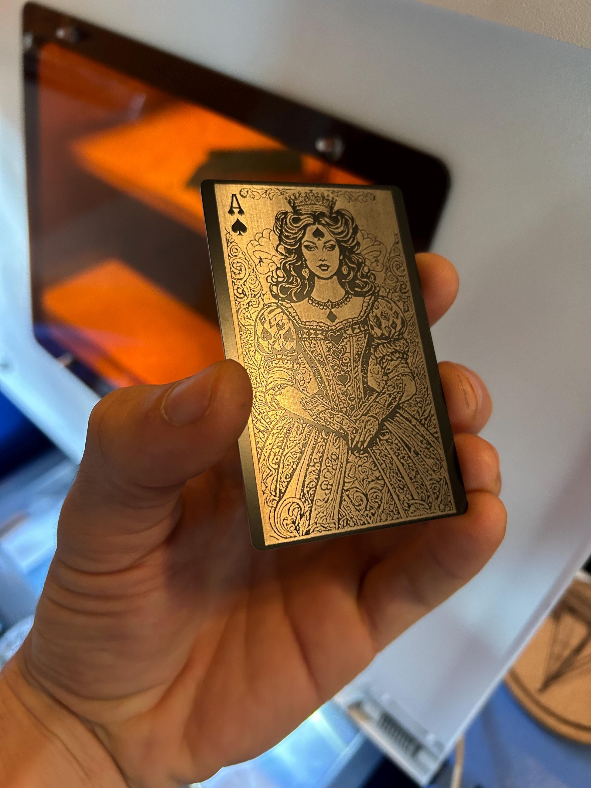 Hand holding a black and silver metal playing card with intricate Lady Luck Ace of Spades design against a blurred background