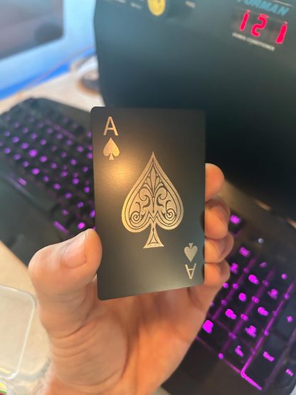 metal poker card with silver ace of spades design in front of a computer keyboard.