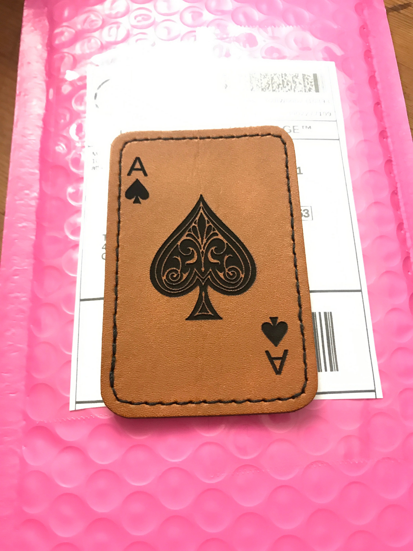 Brown leather patch with black ace of spades design laser engraved on pink bubble wrap