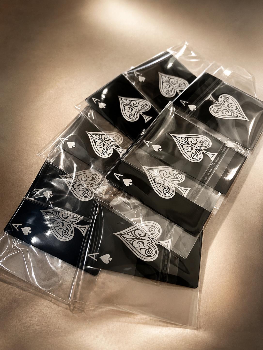 Laser engraved metal ace of spades card packaged in cellophane enclosures for mailing, shown in black/silver anodized aluminum