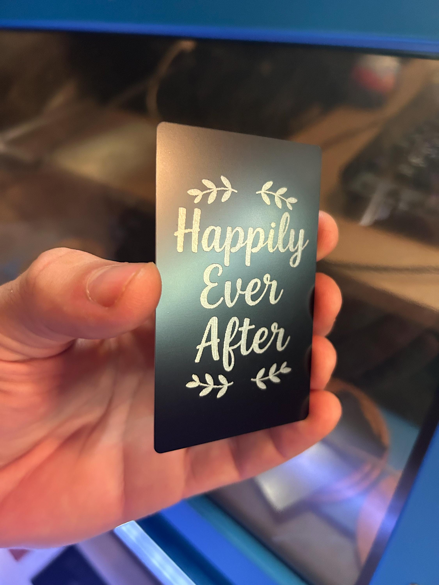 Person holding a laser engraved anniversary gift card in black and silver metal with “Happily Ever After” design