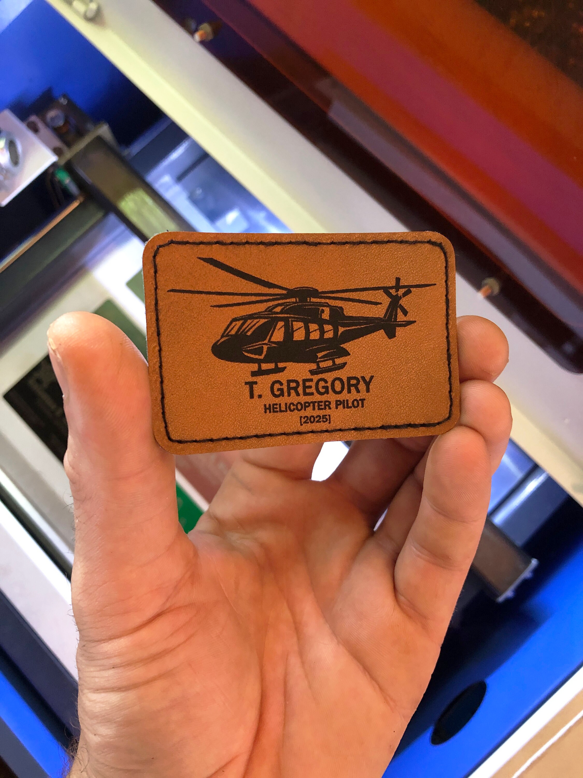 Hand holding a brown leather patch with helicopter pilot certification design and text.