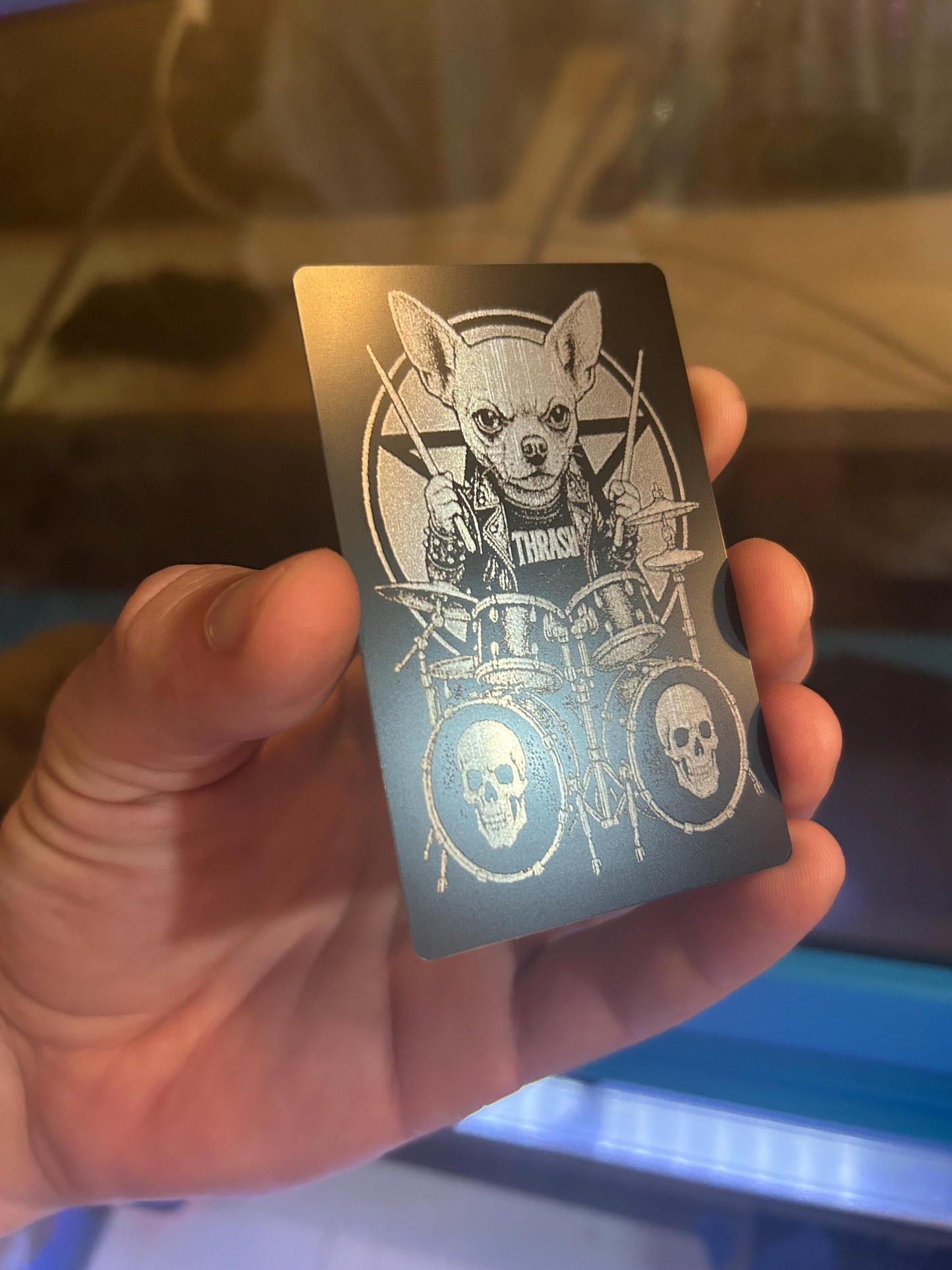 Hand holding a metallic card with a dog rocker graphic illustration laser engraved in anodized aluminum