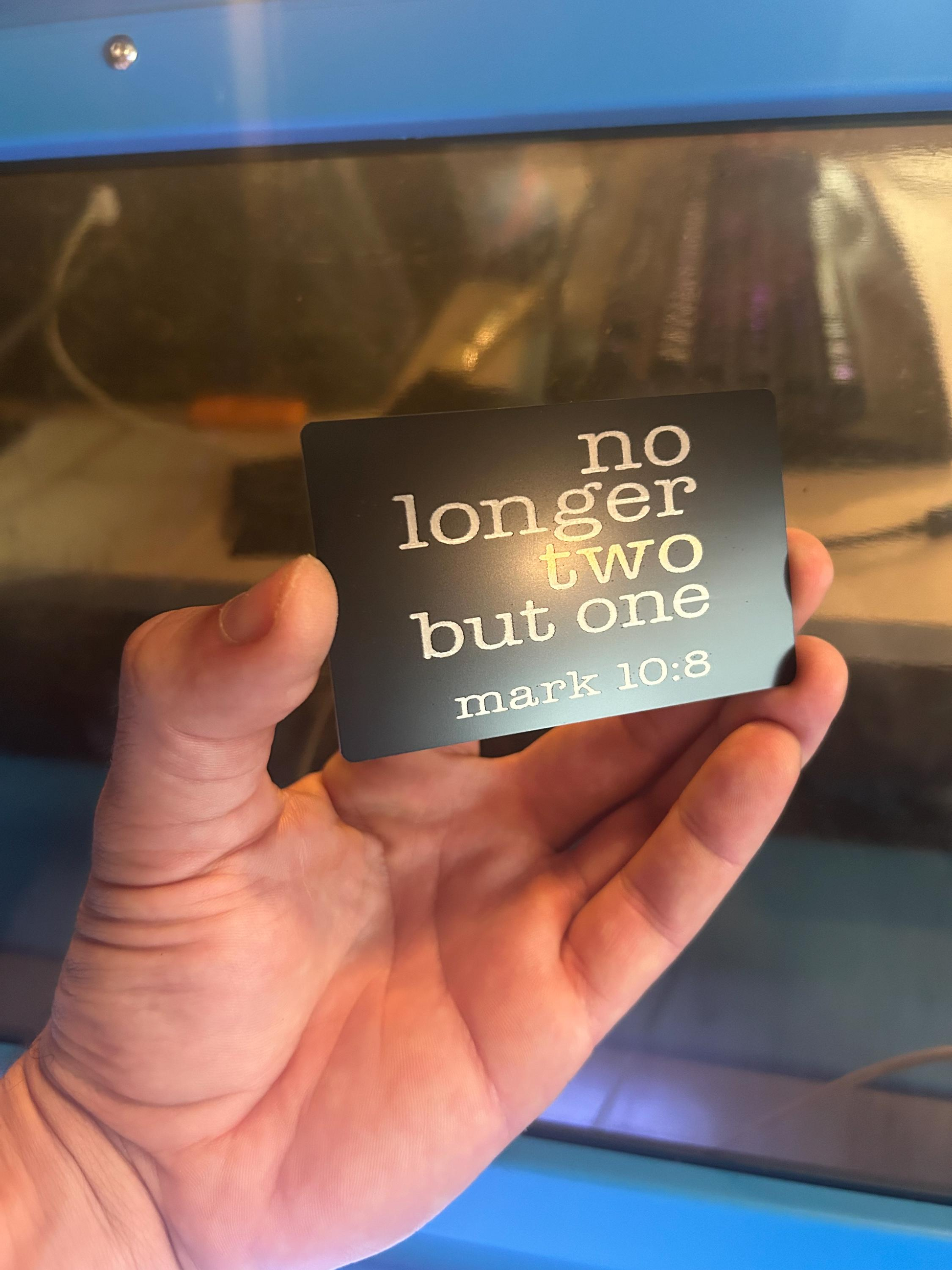 Hand holding a metal card with text 'no longer two but one' from Mark 10:8, gifts for new parents