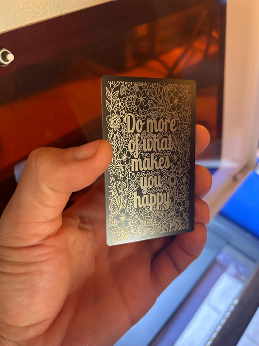 Hand holding a laser engraved motivational keepsake that reads "Do More Of What Makes You Happy" text silhouetted on a floral nature pattern