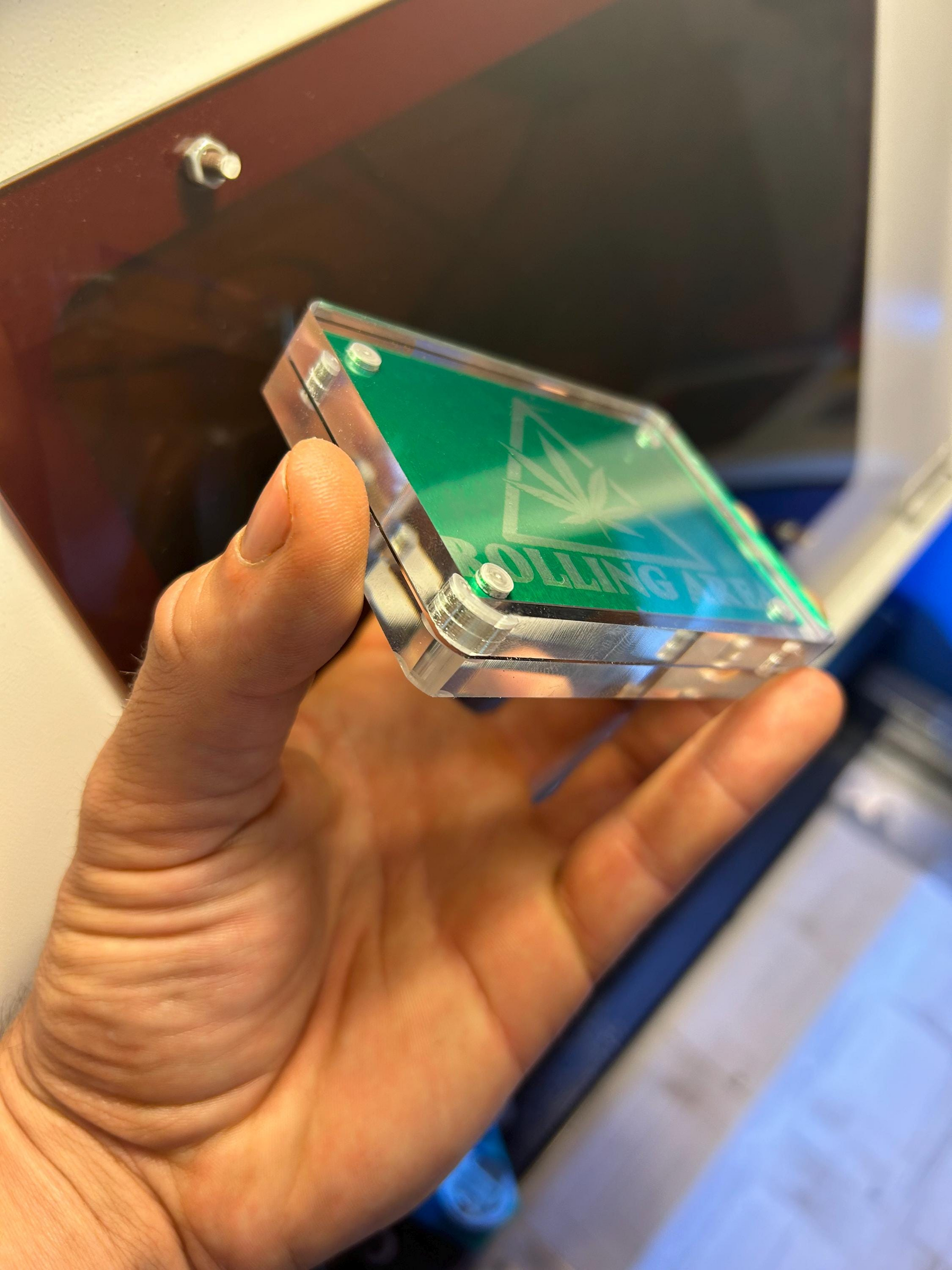 Hand holding a magentic acrylic display case for metal business cards with green/silver laser engraved example