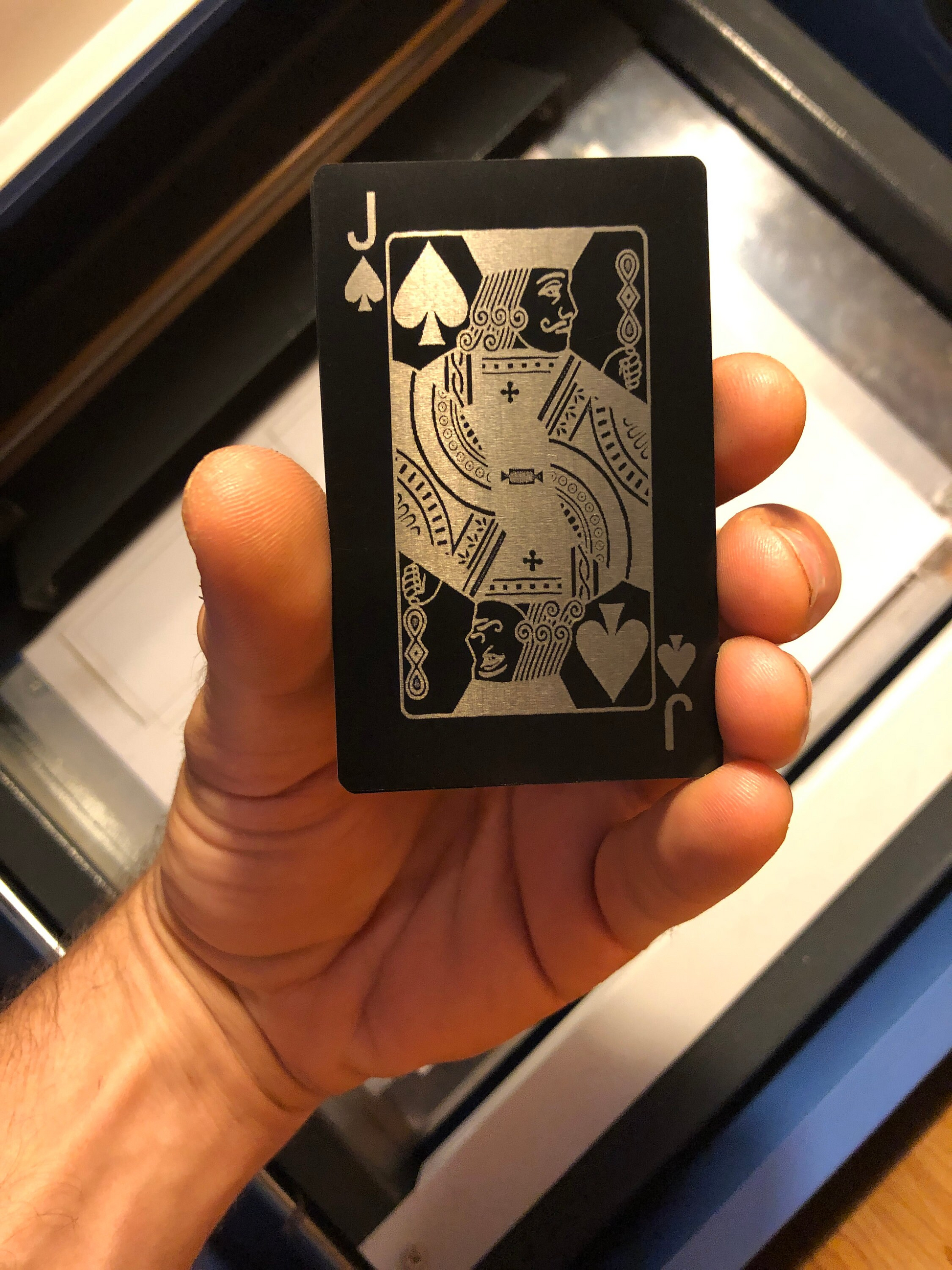 Hand holding a laser engraved metal black and silver playing card with a cnc etched design