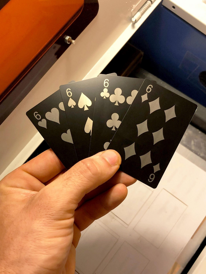 Hand holding a metal six of hearts, six of spades, six of clubs and six of diamonds playing card in front of a machine