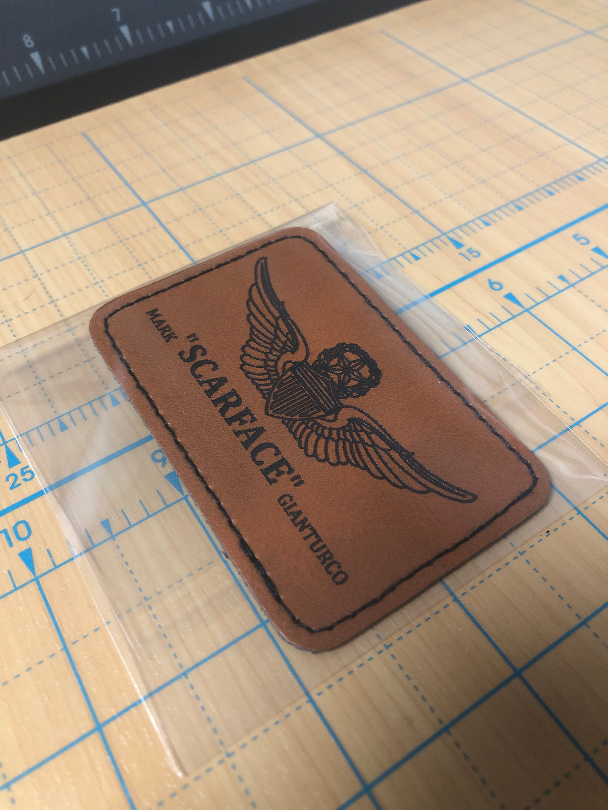 Brown leather patch with nickname, name and flight wings logo on a grid surface
