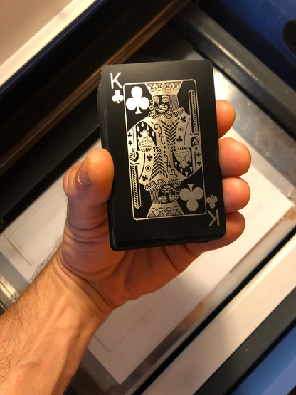 Hand holding a deck of metal black/silver playing cards, with King of Clubs on top
