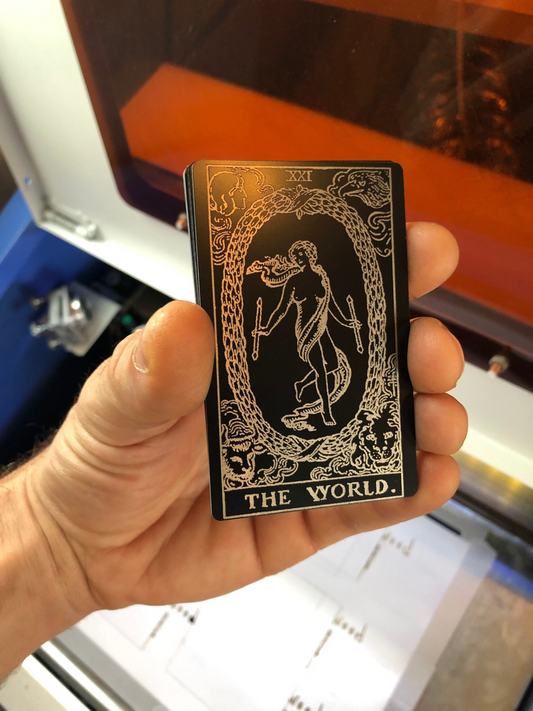 Hand holding a black and silver metal tarot wallet card with 'The World' symbol laser engraved