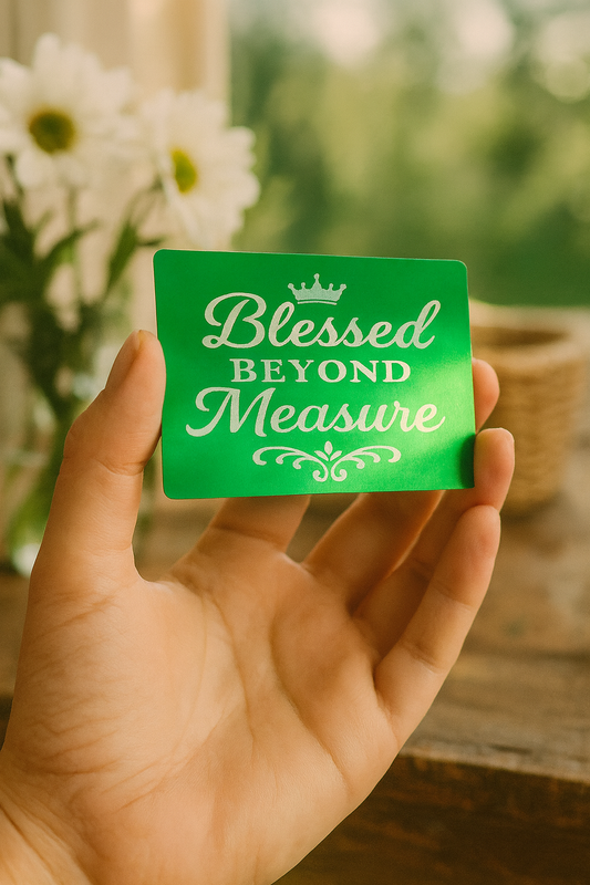 Hand holding a green/silver laser engraved metal keepsake card with 'Blessed Beyond Measure' text against a blurred natural background