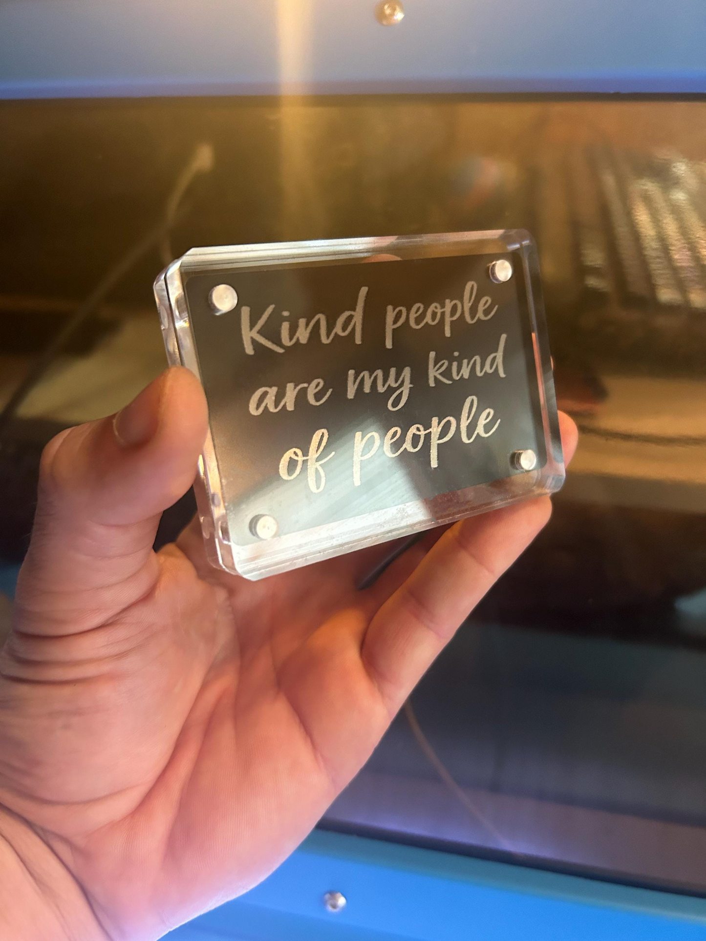 Hand holding a clear square acrylic display case with engraved text.