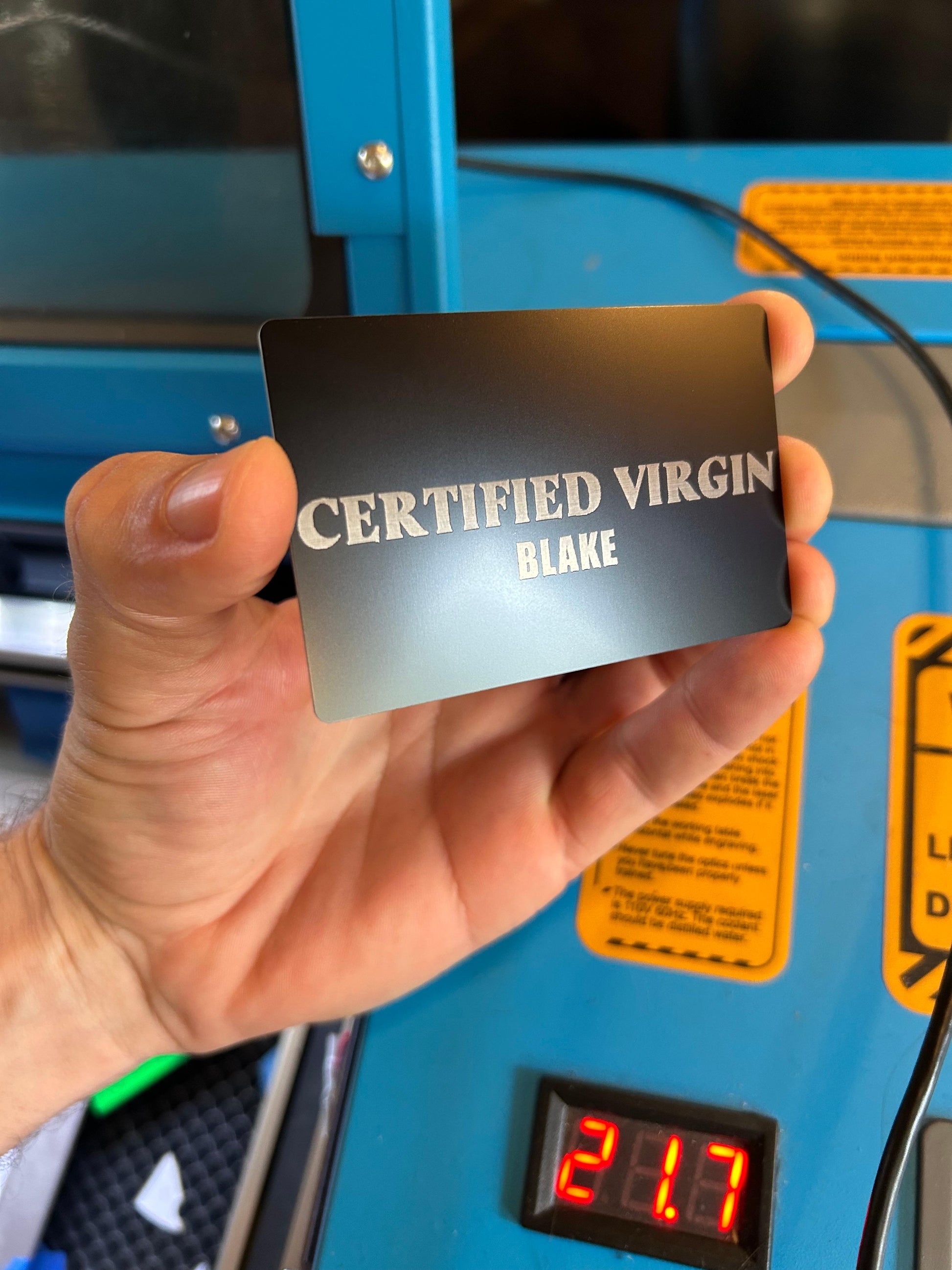 Metal gag gift card with 'Certified Virgin' and personalized name engraving text in black/silver