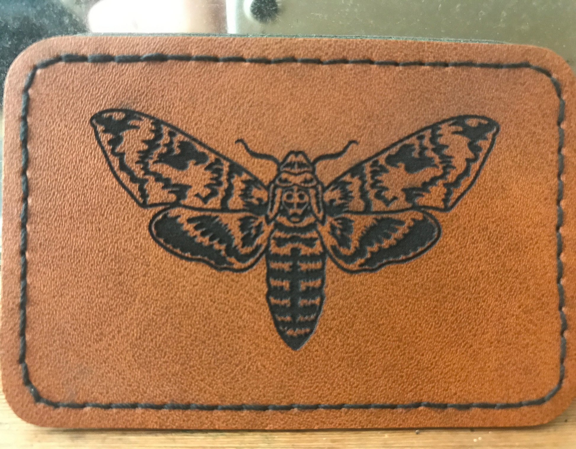 Brown leather Cicada heat activated adhseive backed patch on a wooden surface