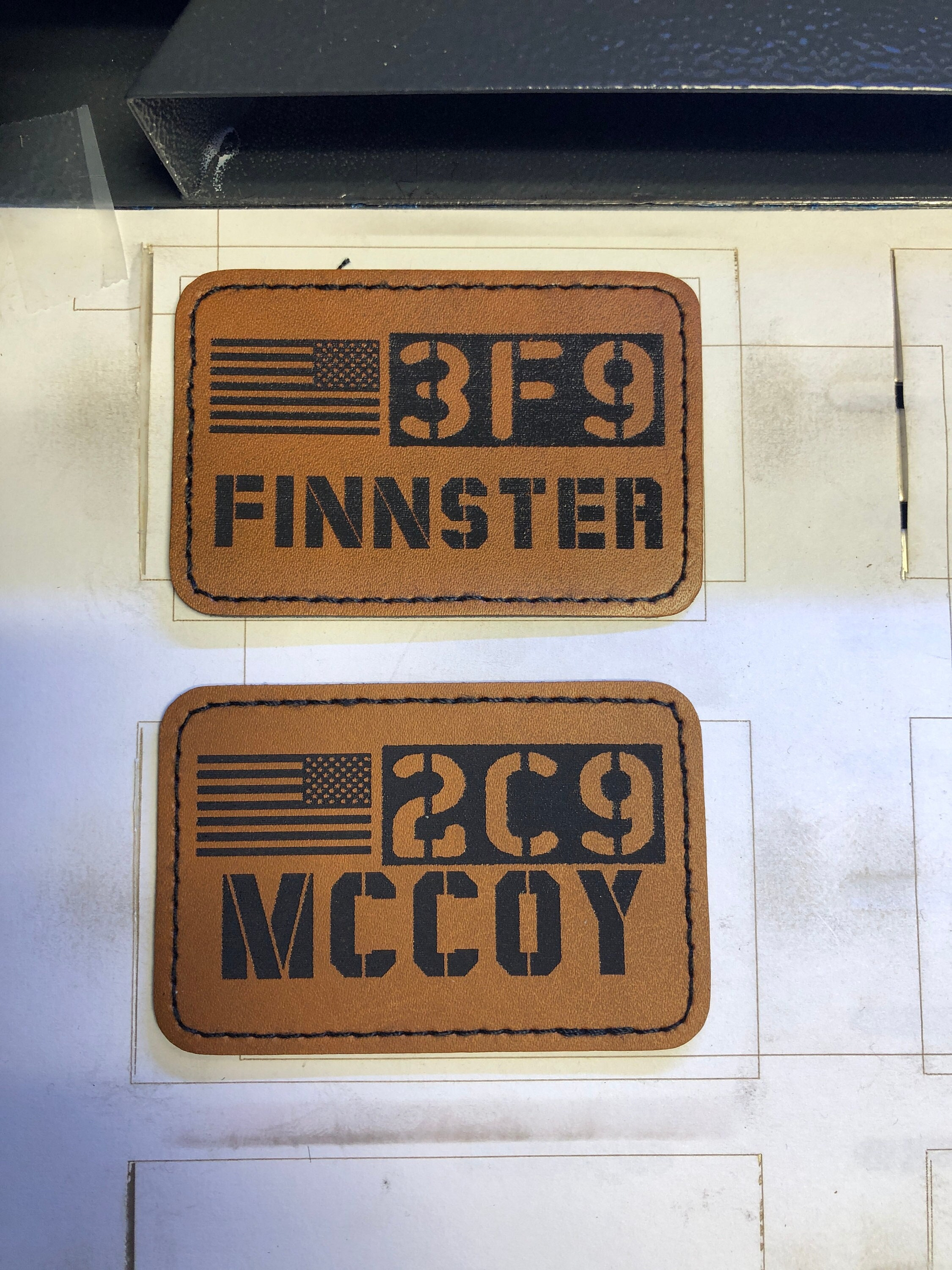 Two brown leather patches with Call Sign engravings and an American flag design on a white background.