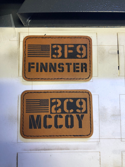 Two brown leather patches with Call Sign engravings and an American flag design on a white background.