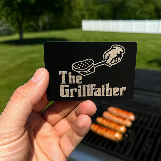 Card with 'The Grillfather' design held by a hand, with a grill and sausages in the background.