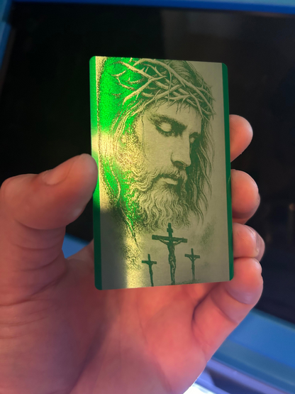Hand holding a metal green card with a religious design featuring jesus and crucifix.