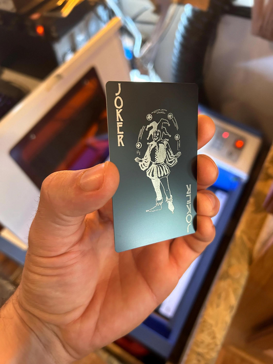 Hand holding a black card with white design and text, blurred production shop background
