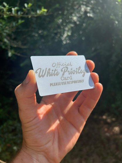 Hand holding a metal wallet insert card with 'Official White Privilege Card' sarcastic pop culture reference against a blurred natural background