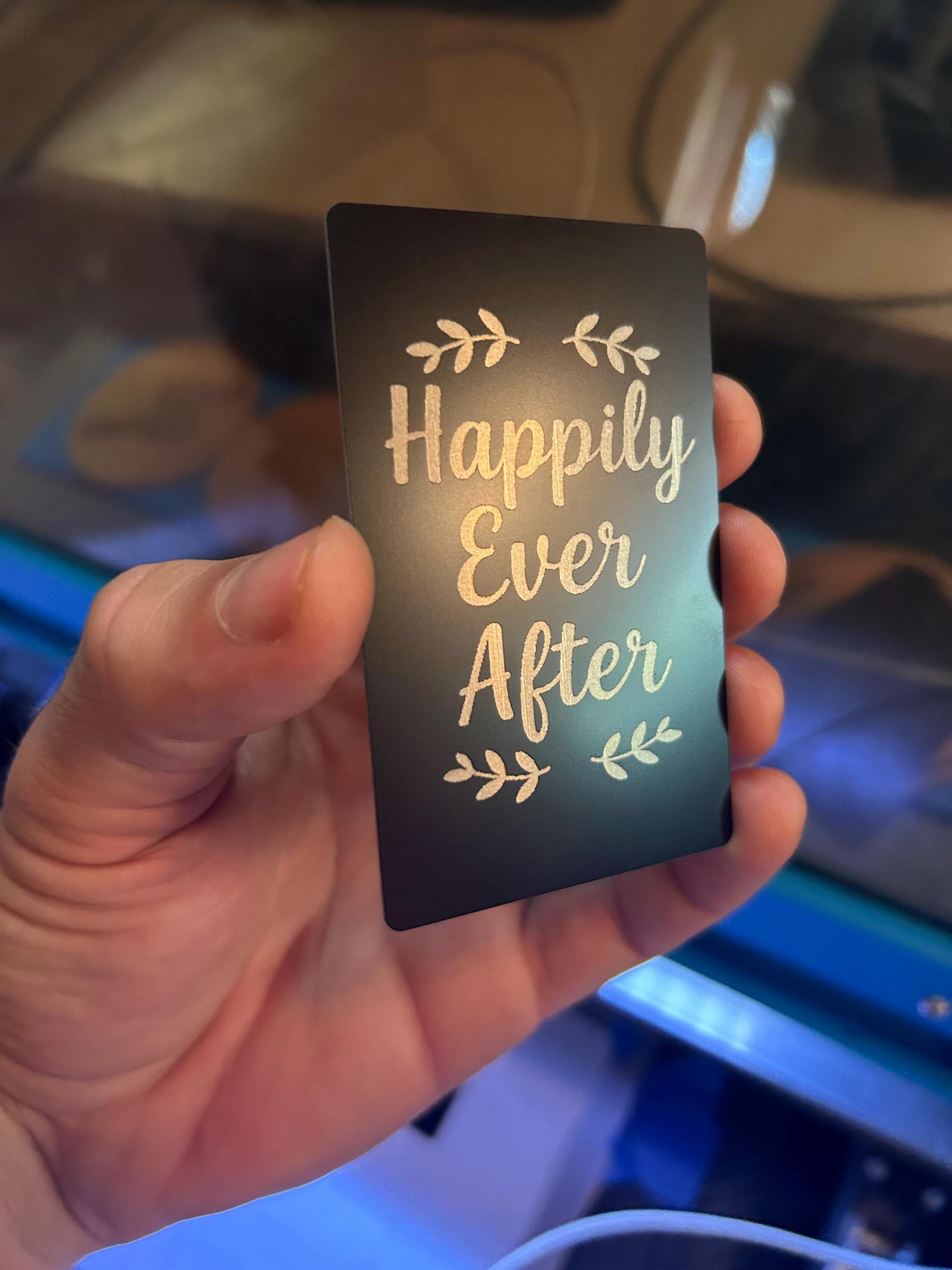 Hand holding a laser engraved black and silver metal couples keepsake card with “Happily Ever After” typography design