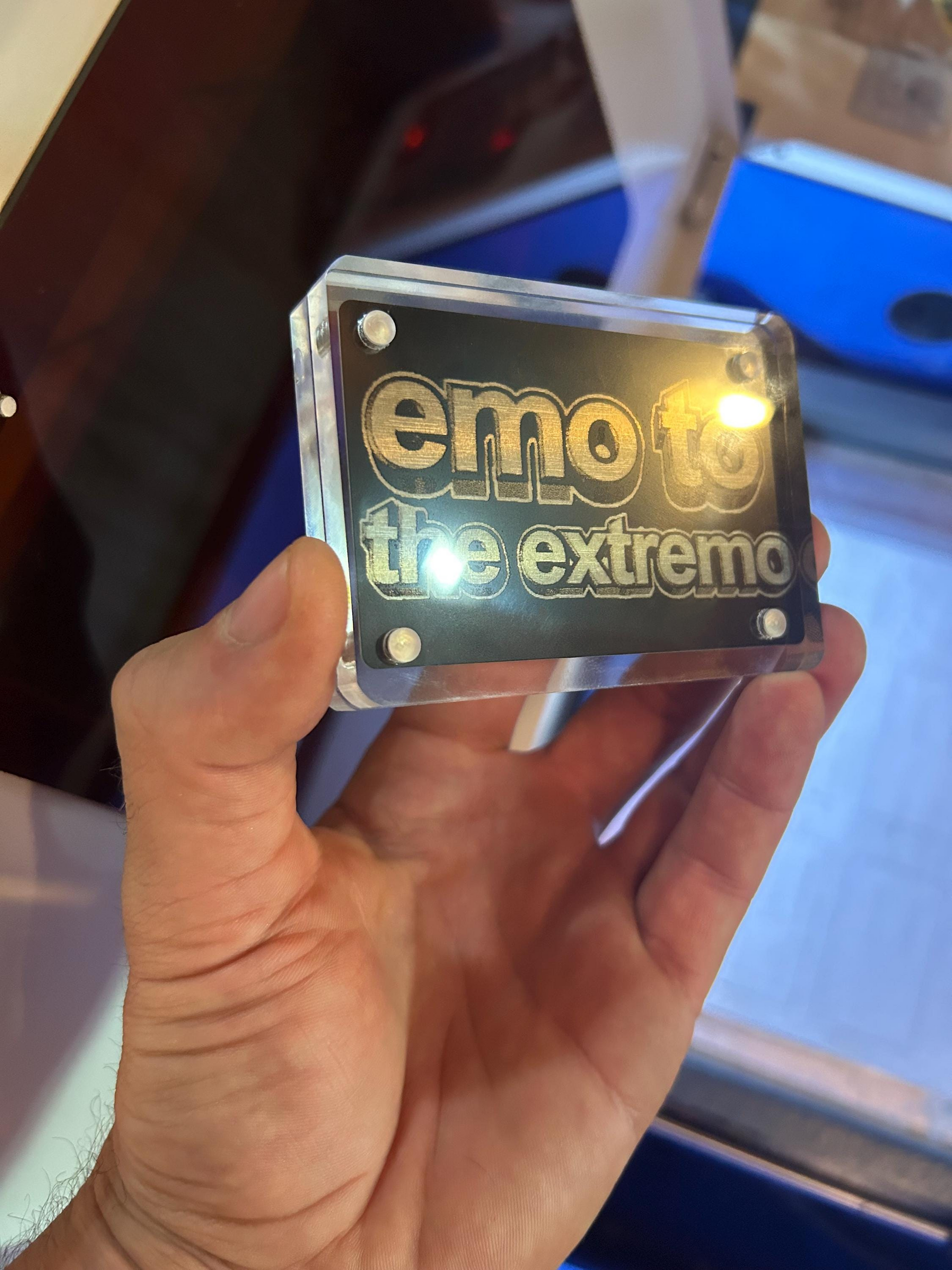 Hand holding an acrylic display with demonstration laser engraved "emo" card inside