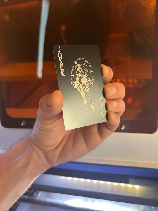 Hand holding a silver card with branding against a laser engraving machine tray