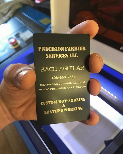 Hand holding a metal business card for custom text laser engraved for a small business farrier company with contact information.