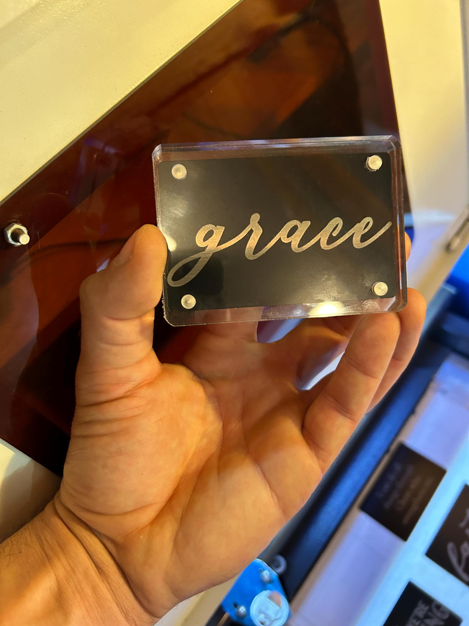 Hand holding a clear acrylic display case, with metal keepsake card 'grace' inside