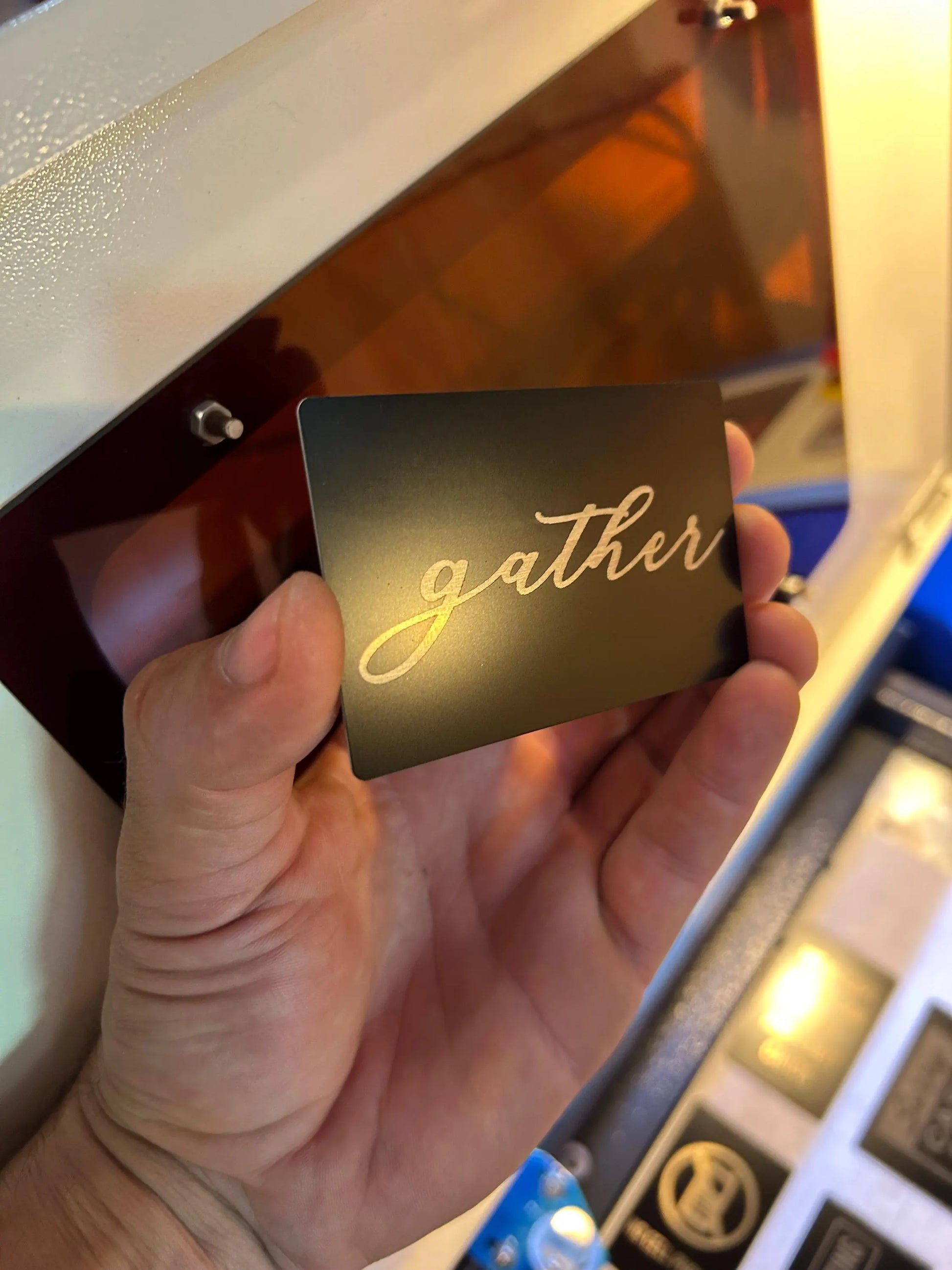 Hand holding a metal mini placard with 'gather' laser engraved on it